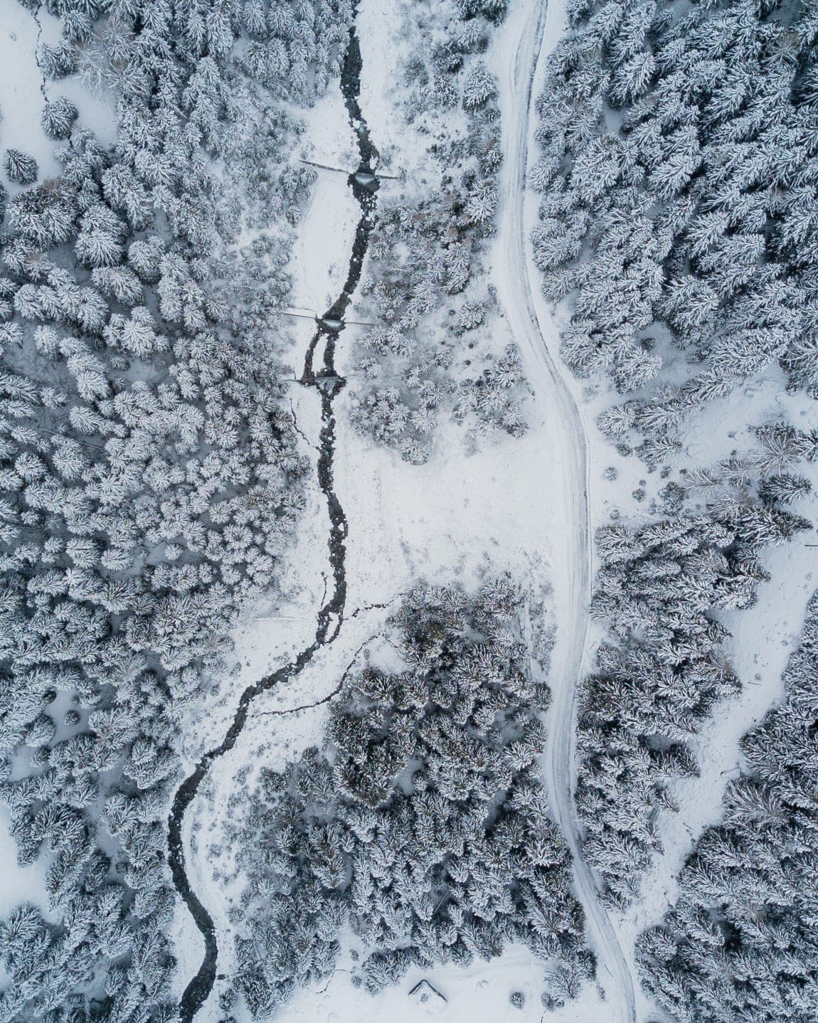 An aerial view looking down onto a frozen valley floor laced with pale ice and dark rock in Graubünden.