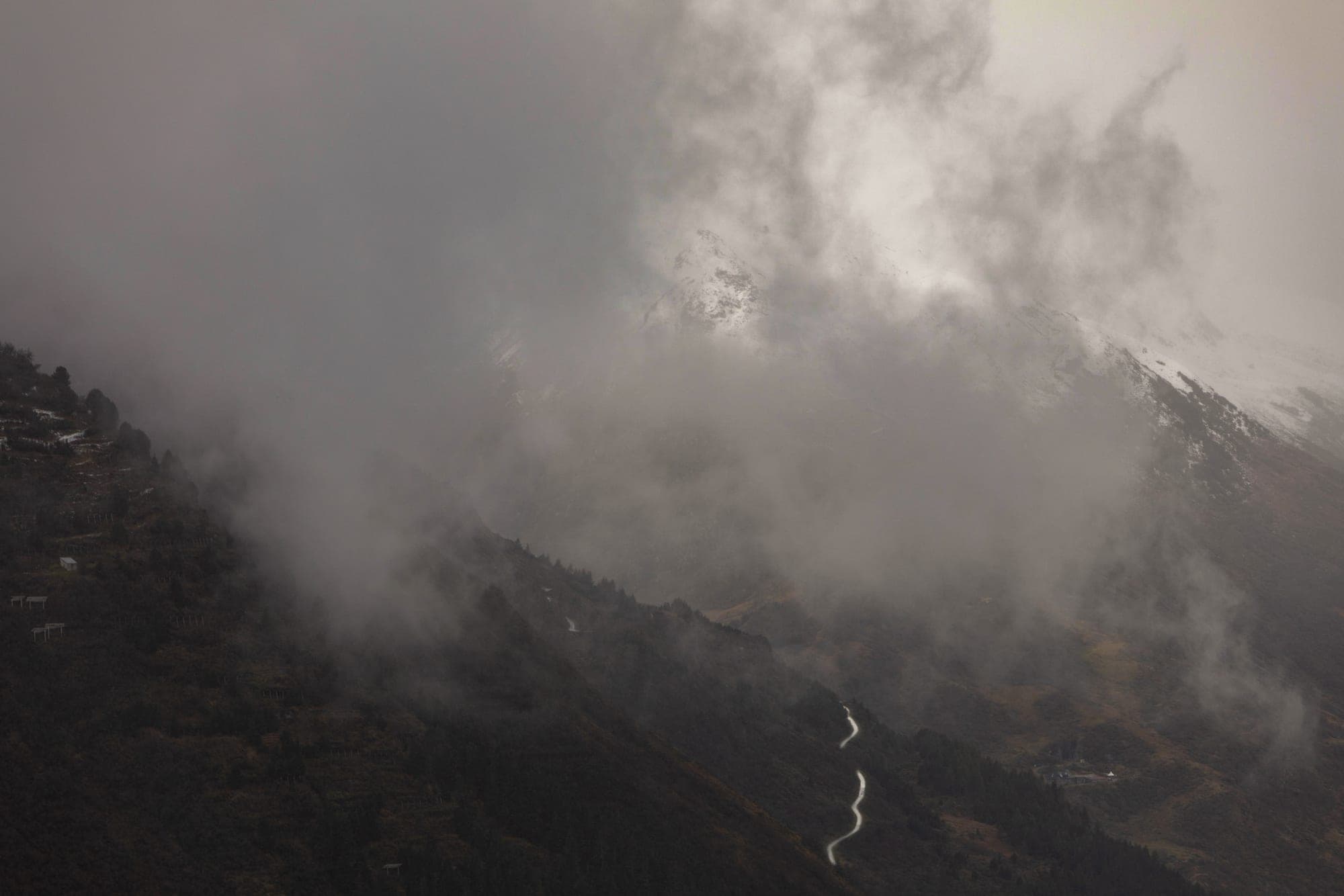 A switchback road emerging from breaking cloud above a mist-filled valley in Graubünden.