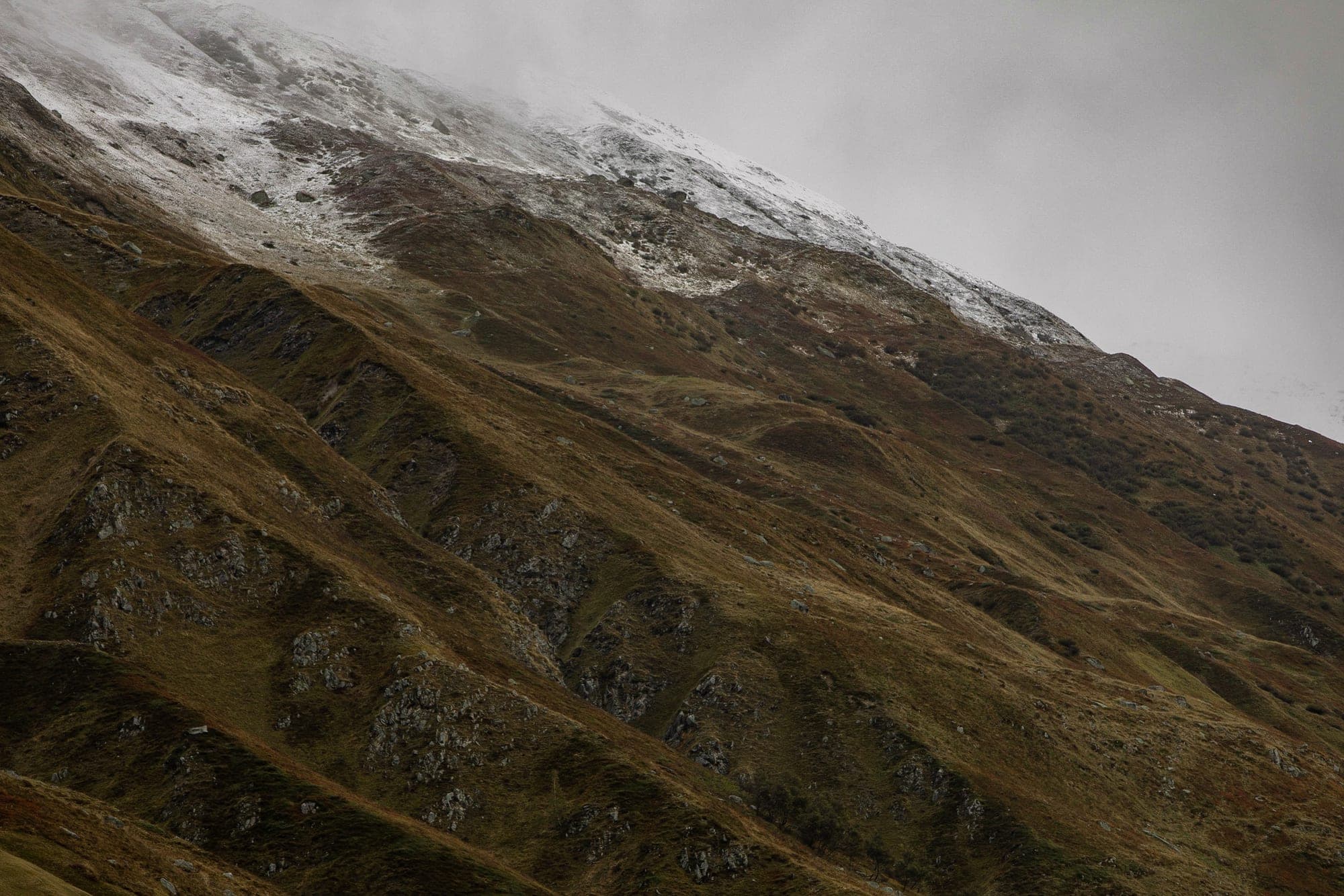 A high mountain ridge of dark scree streaked with snow under a pale sky in Wallis.