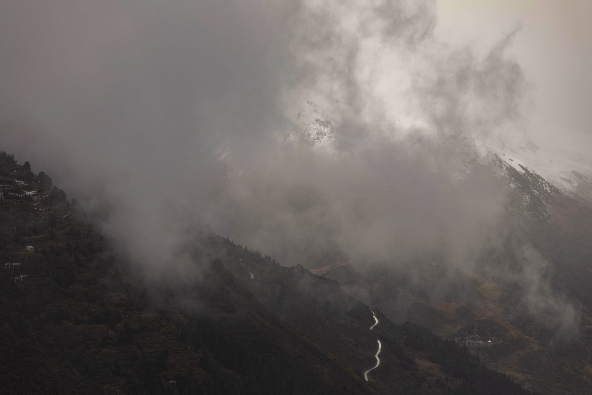 A switchback road emerging from breaking cloud above a mist-filled valley in Graubünden.